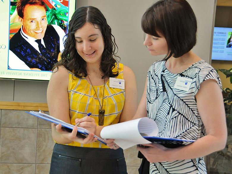 two staff members looking at their clipboards and laughing together in centre hall